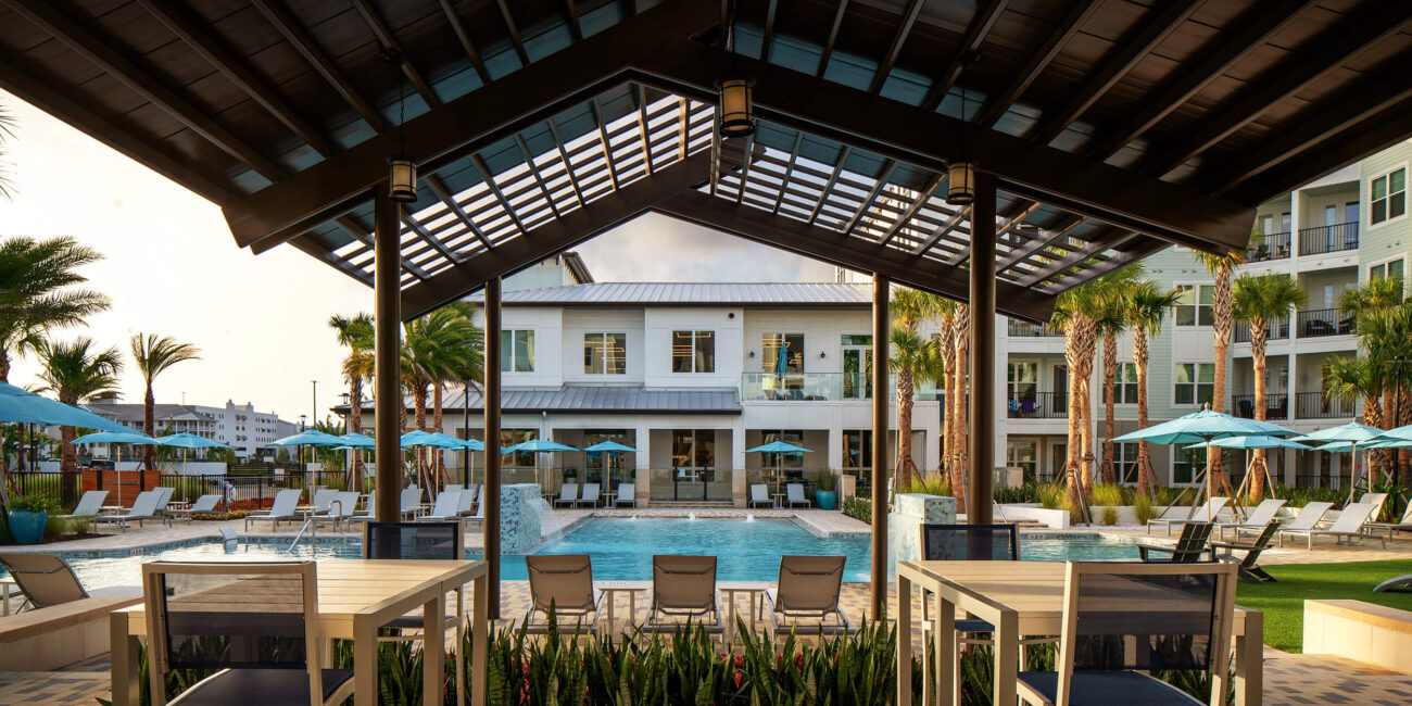 Bainbridge at Westshore Marina covered lounge area with tables and chairs near pool and multistory building in the back